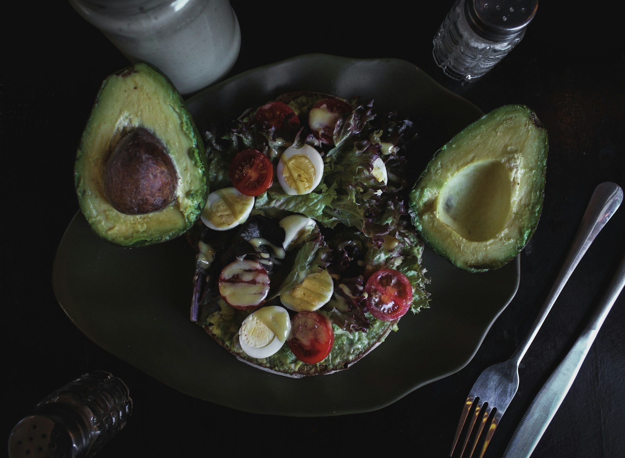 An avocado toast plate with soft-boiled eggs and salad greens, shot in moody natural light